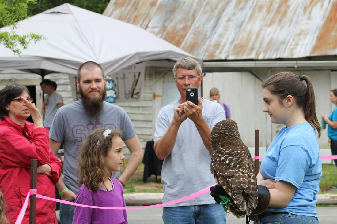 A woman holding an owl stands in front of a group of people.